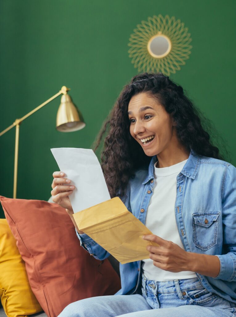 Happy woman at home with holding message envelope sitting on sofa in living room.